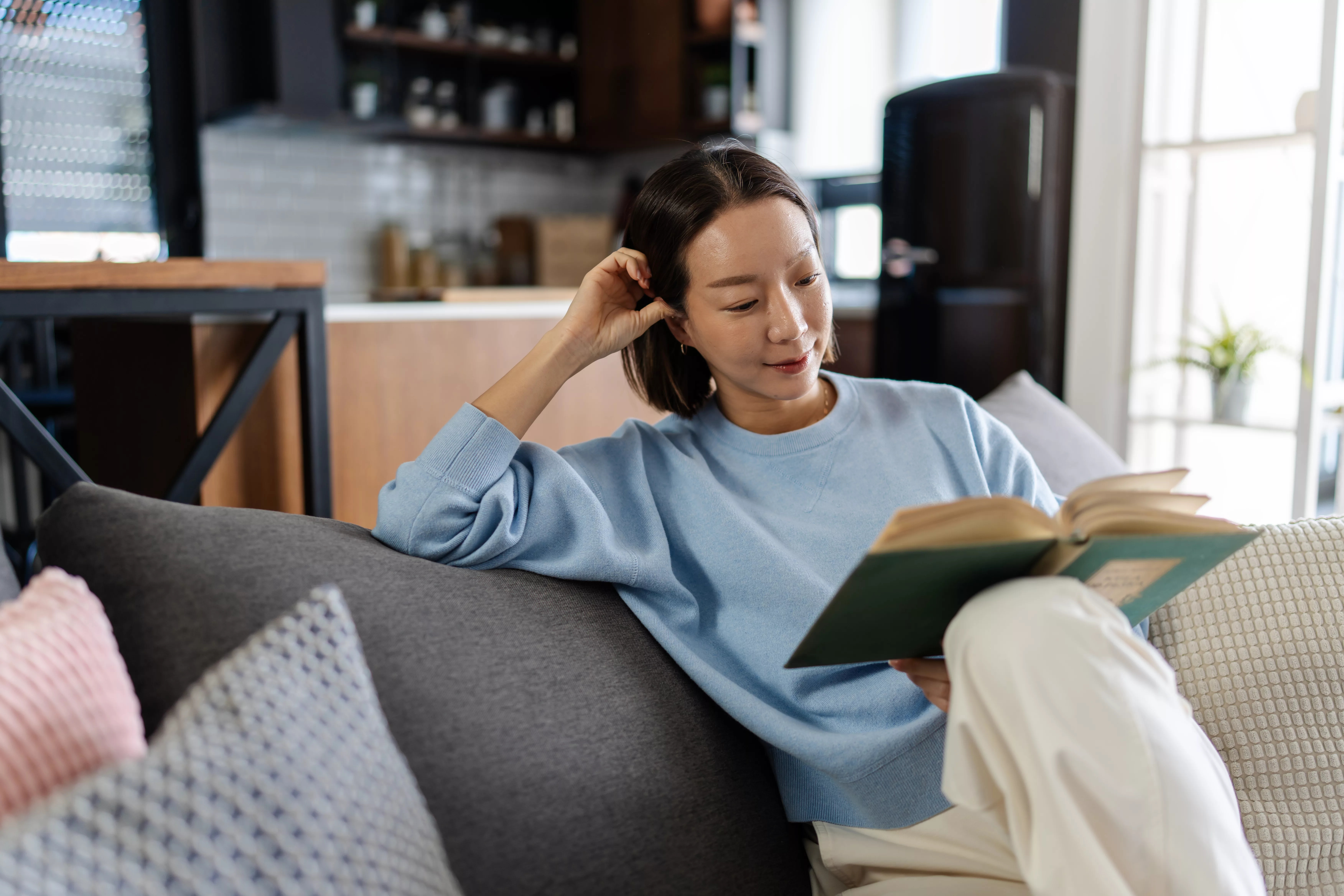Woman reading a book on a sofa, smiling.
