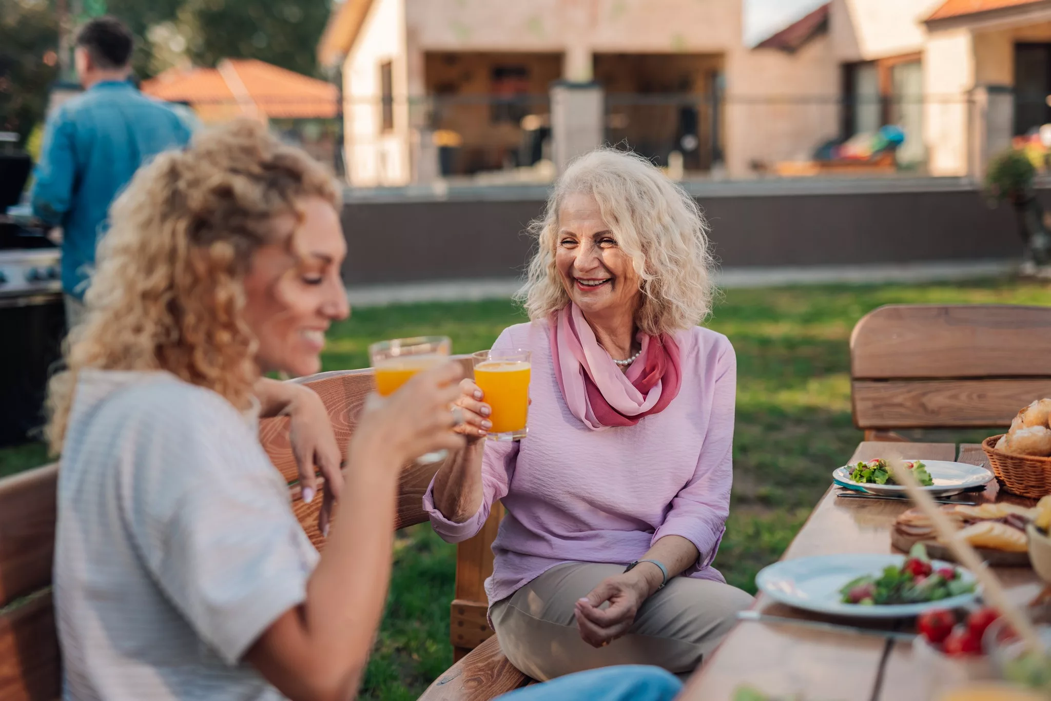 Younger and elder woman clinking glasses in a garden.